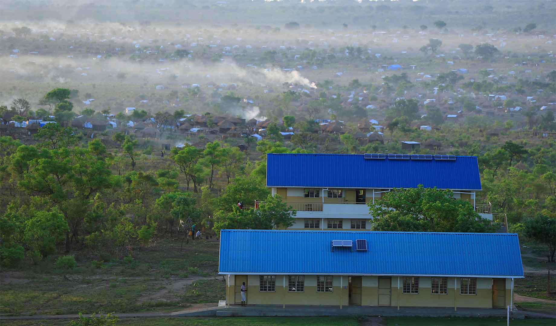 An aerial view of Bidi Bidi refugee settlement taken on 5 April 2017 amid the arrival of South Sudanese families fleeing war. In the foreground we see a building with a blue roof. In the backdrop dozens of tents. 